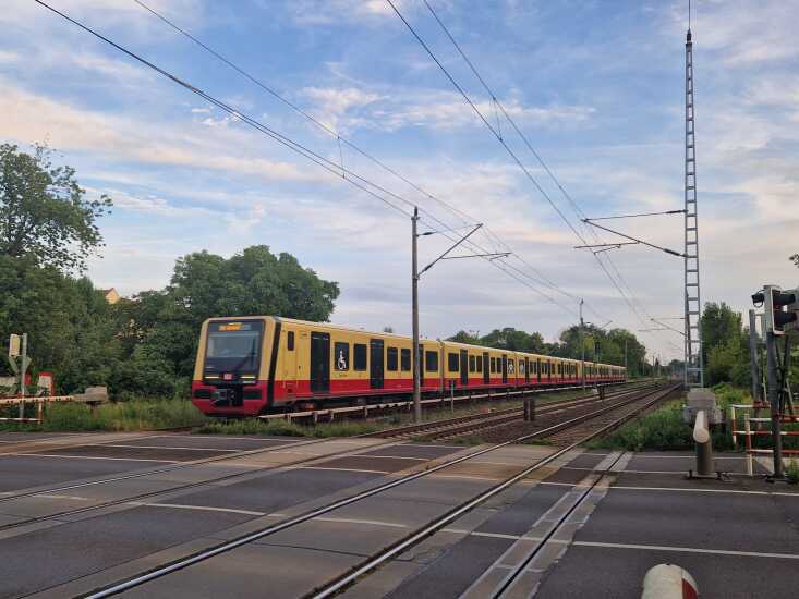 Eine leicht idyllisch anmutende Szene einer S-Bahn an einem Bahnübergang in Wildau