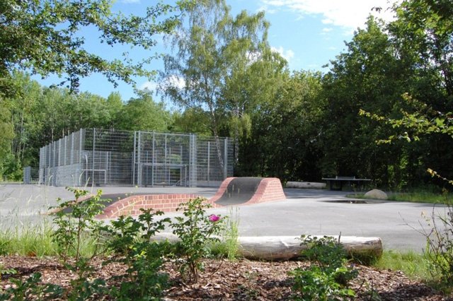 Eingezäunter Bolzplatz mit hohen Zäunen, davor Skate-Rampen