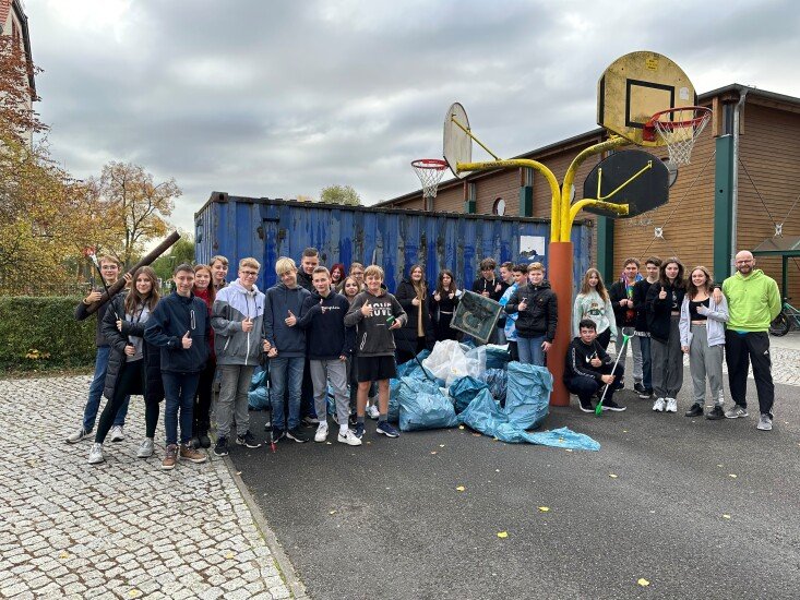 Gruppe von Schülern vor einem blauen Container mit gesammeltem Müll