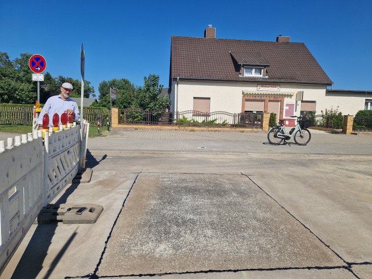 Herr Nerlich steht an einem Straßenabsperrgitter in der Sonne